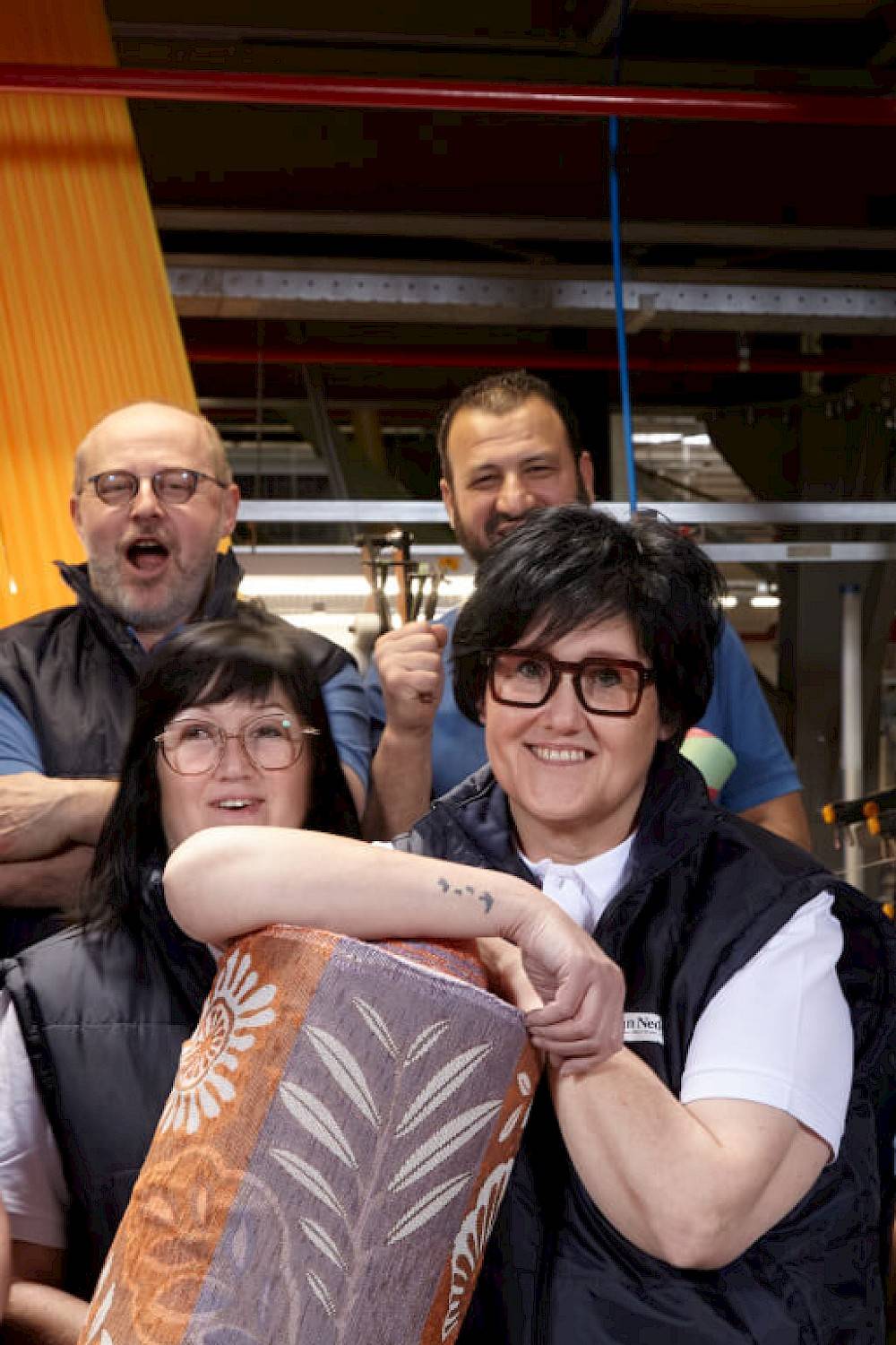 four joyous employees Weverij Van Neder - person in front holding a roll of fabric