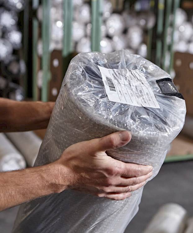 Hands holding a large wrapped roll of cloth packed in plastic